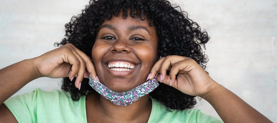 Happy Afro woman portrait - African girl wearing face mask smiling in front of camera - Health care and corona virus outbreak concept