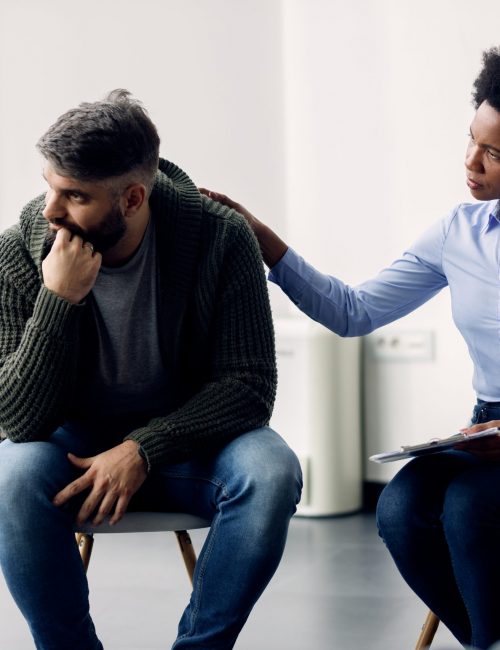 Black female therapist supporting a man who is talking abut his issues during group meeting. African American psychotherapist encouraging a man to talking about his problems during group therapy.