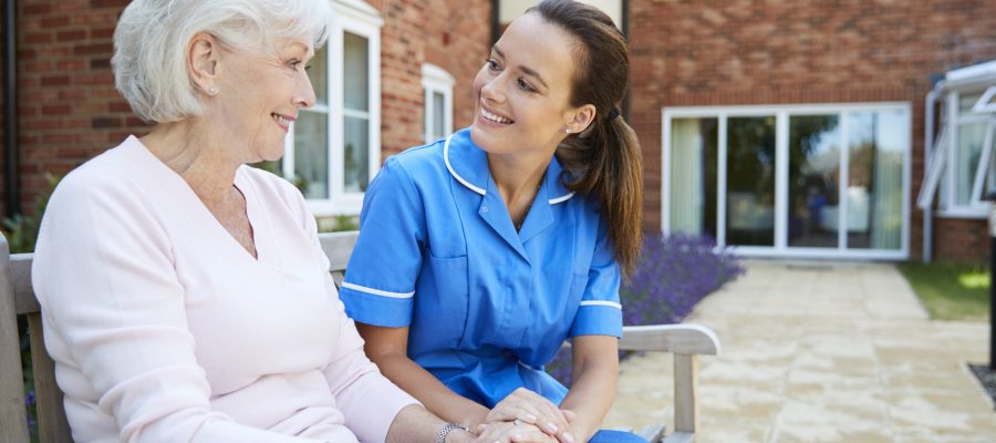 Senior Woman Sitting On Bench And Talking With Nurse In Retirement Home Senior Woman Sitting On Bench And Talking With Nurse In Retirement Home