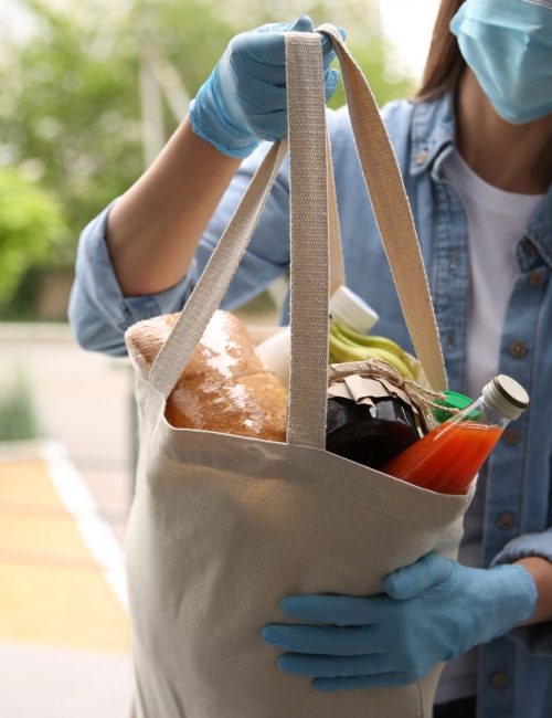 Female volunteer giving bag with products through doorway, closeup. Aid during coronavirus quarantine Female volunteer giving bag with products through doorway, closeup. Aid during coronavirus quarantine